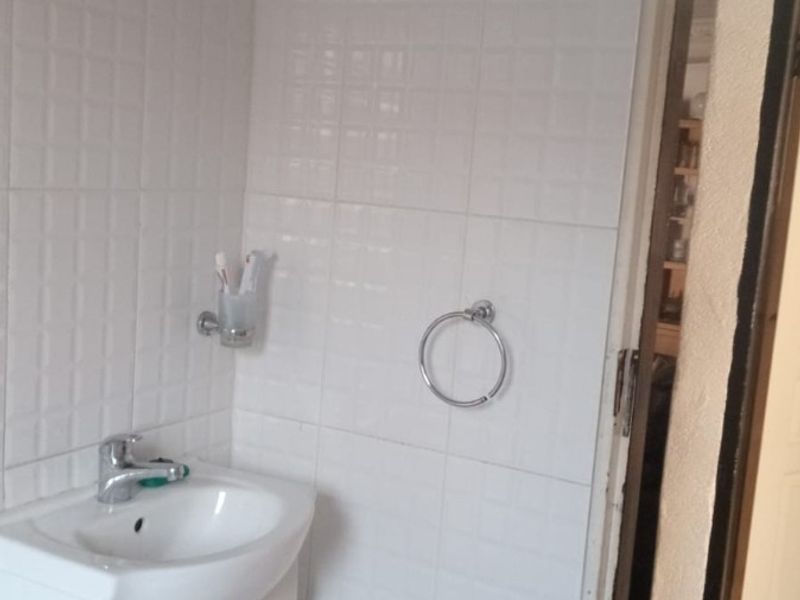 A functional bathroom featuring a white vanity cabinet with a basin, chrome fixtures, and full-height white wall tiling.