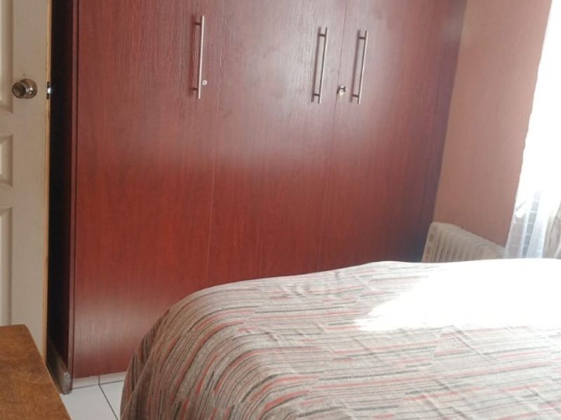 A bedroom featuring a large built-in wooden wardrobe, tiled flooring, and decorative ceiling cornicing.