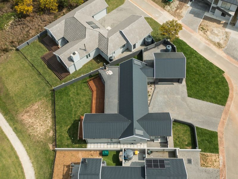 Aerial view of a modern residential property featuring metal roofing, solar panels, timber decking, and a paved driveway within a landscaped estate.