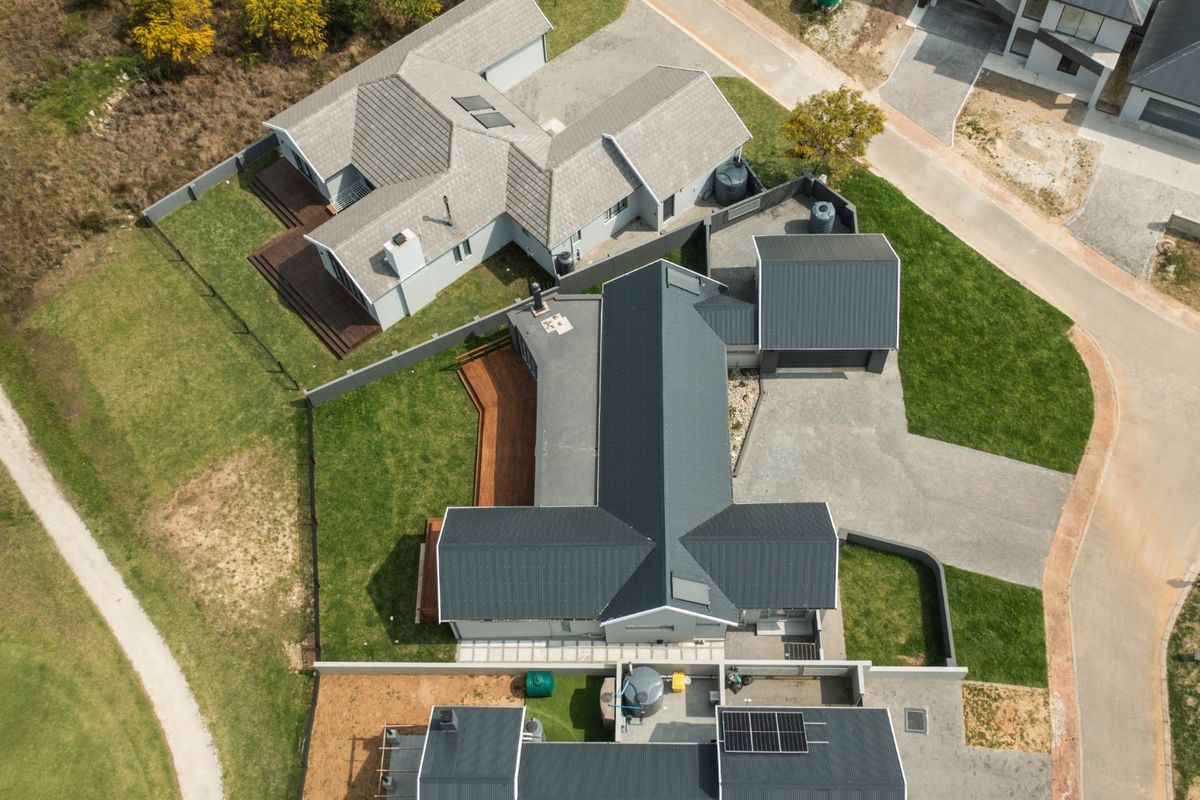 Aerial view of a modern residential property featuring metal roofing, solar panels, timber decking, and a paved driveway within a landscaped estate.