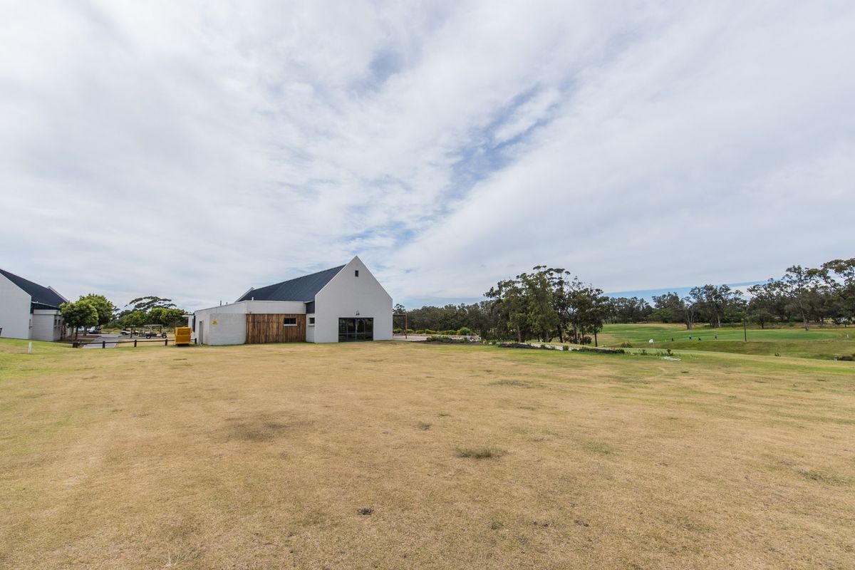 A wide-angle view of the rear exterior of a modern farmhouse-style property featuring a pitched roof, timber accents, and expansive surrounding lawn.
