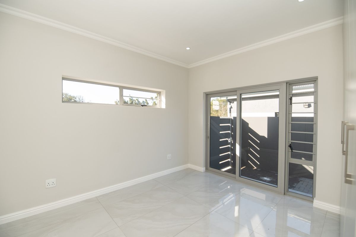 A bright, empty bedroom featuring modern tiled flooring, neutral walls, recessed lighting, and a sliding glass door providing access to the exterior.
