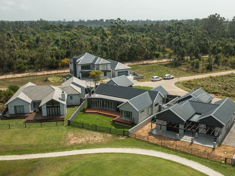 Aerial view of a modern residential estate featuring multiple homes with metal roofs, timber decks, and landscaped surroundings in a scenic setting.