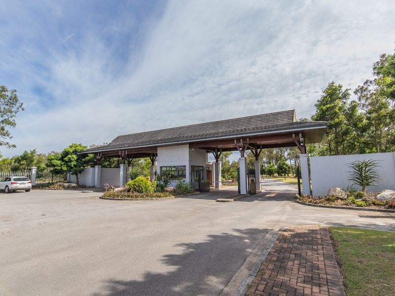 A well-maintained security gatehouse entrance for the estate, featuring a timber-framed roof structure, paved driveway, and secure access control.