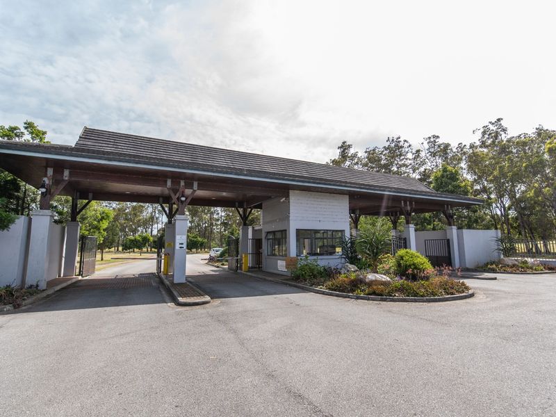 A well-maintained security gatehouse entrance featuring a covered driveway, timber structural elements, and landscaped garden beds.