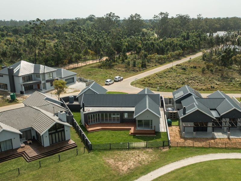 Aerial view of a modern residential estate featuring multiple detached homes with pitched metal roofs, timber decks, and landscaped surroundings.