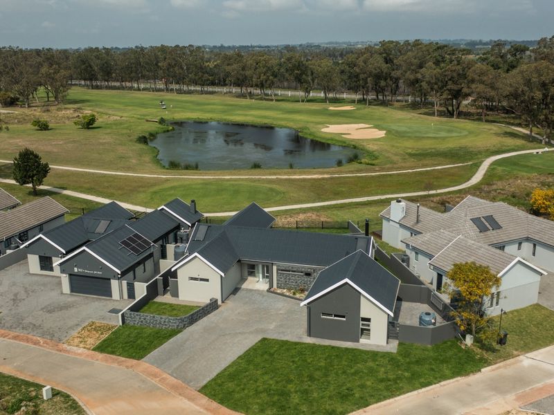 Aerial view of a modern residential property featuring multiple pitched roof structures, paved driveways, and solar panels, situated adjacent to a golf course.