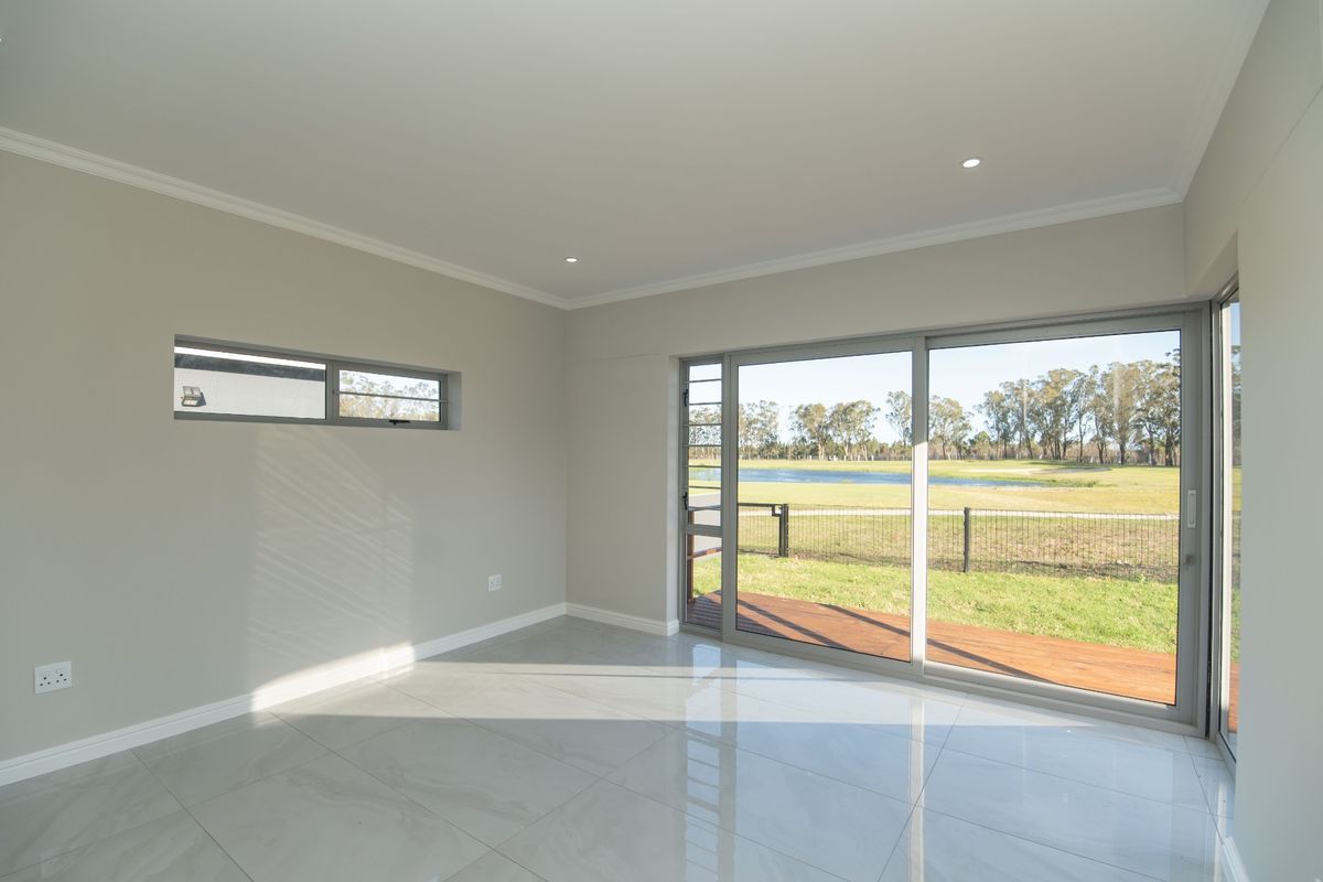 A bright, empty living room featuring large sliding glass doors that open onto a wooden deck with scenic golf course views.