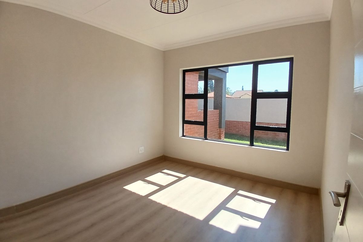 A bright and modern empty bedroom featuring light-toned laminate flooring, neutral walls, and large black aluminium windows.