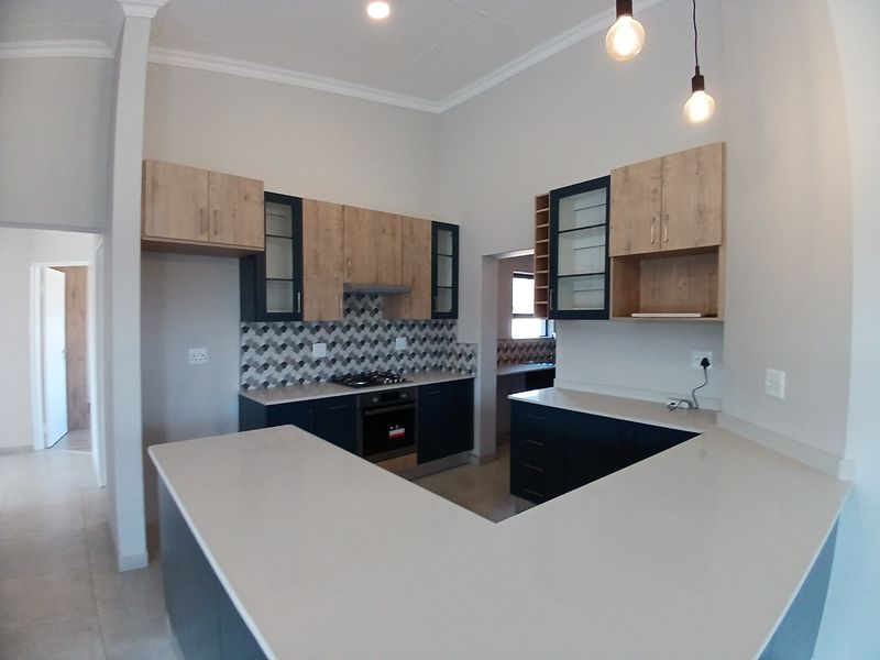 Modern kitchen featuring two-tone cabinetry, stone countertops, gas hob, built-in oven, and a stylish geometric tiled backsplash with ample workspace.