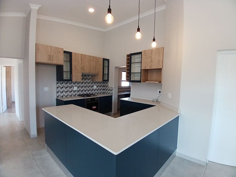 Modern kitchen featuring U-shaped stone countertops, two-tone cabinetry, built-in oven and gas hob, and stylish pendant lighting in an open-plan layout.