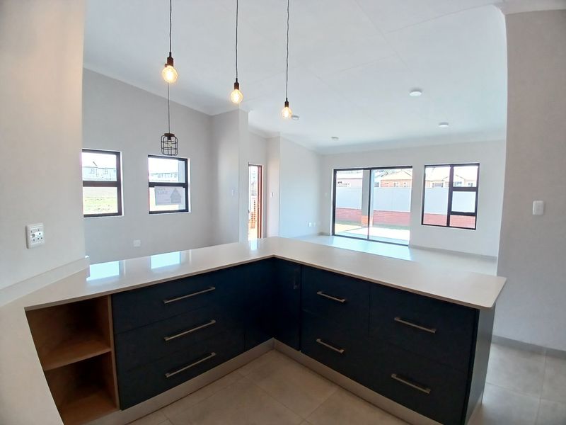 Modern open-plan kitchen and living area featuring dark cabinetry, stone countertops, pendant lighting, and large sliding doors leading to the exterior.