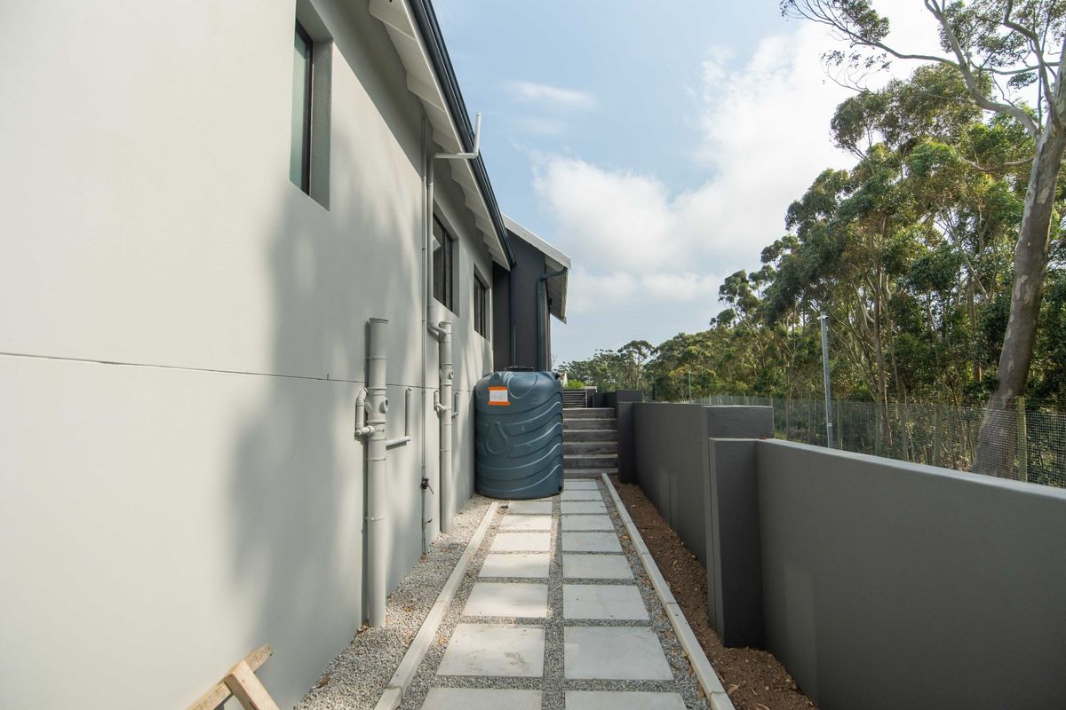 A side exterior pathway featuring a concrete paver walkway, boundary wall, and a water storage tank installed against the house exterior.