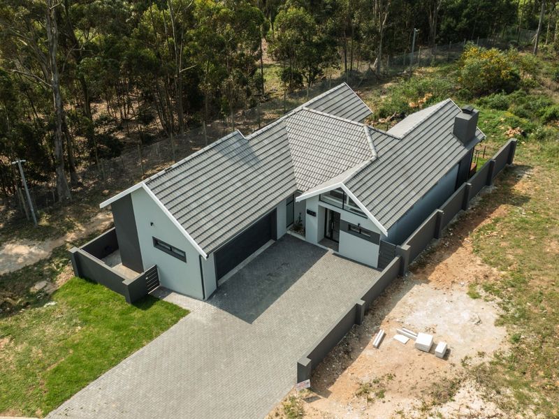 Aerial view of a modern residential property featuring a tiled roof, paved driveway, and perimeter wall, set within a natural wooded environment.
