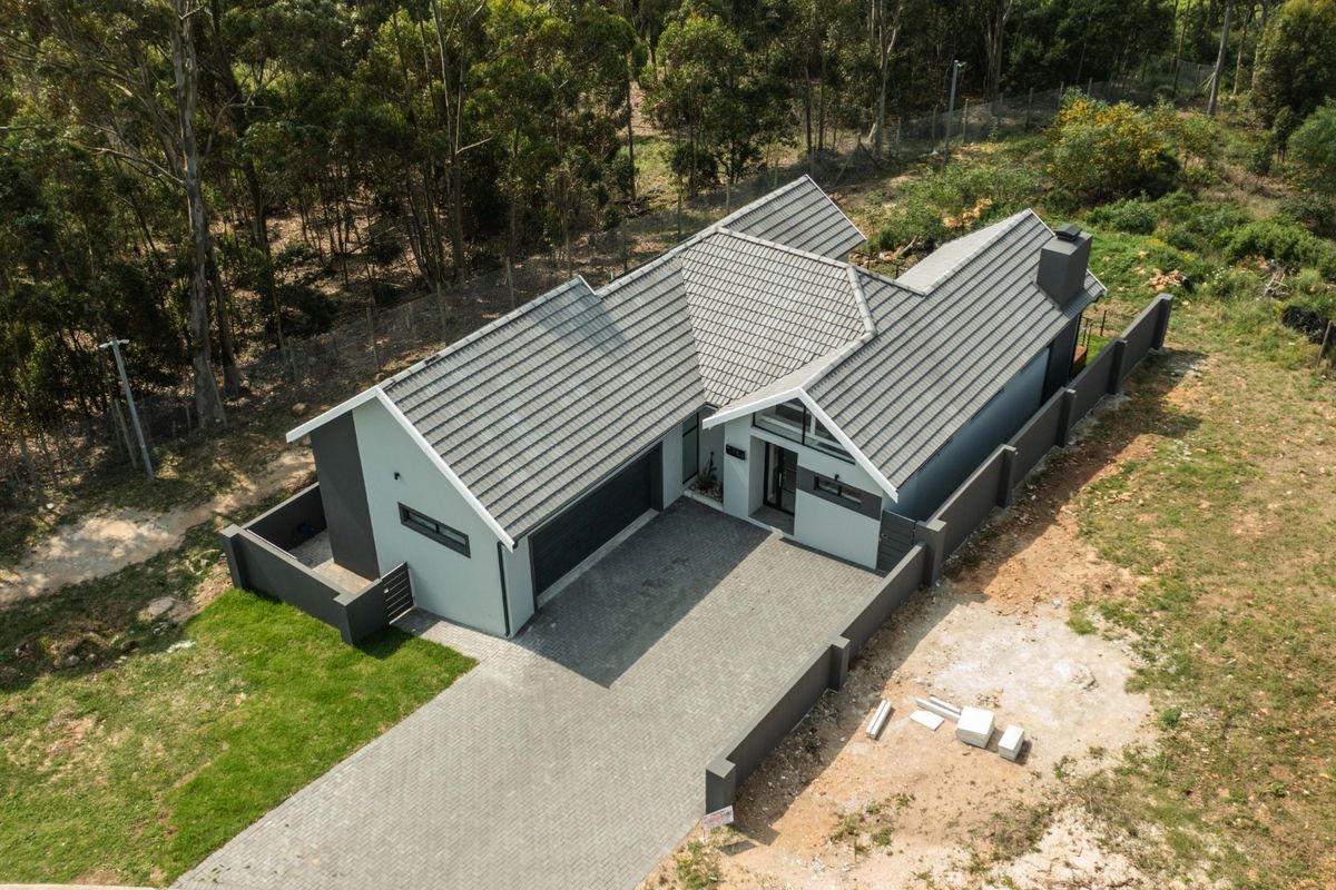 Aerial view of a modern residential property featuring a tiled roof, paved driveway, and perimeter wall, set within a natural wooded environment.