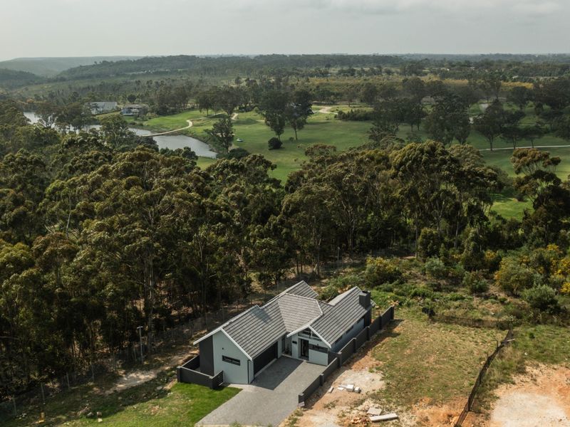 Aerial view of a modern house with a tiled roof and paved driveway, situated in a scenic, wooded estate setting.