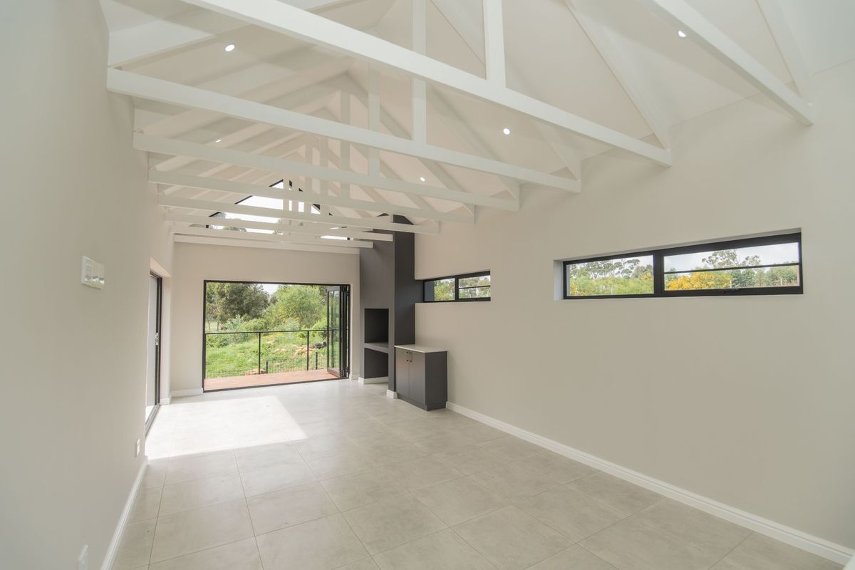 Spacious living area featuring a high vaulted ceiling with exposed trusses, tiled flooring, built-in fireplace, and large bi-fold doors opening to the outdoors.