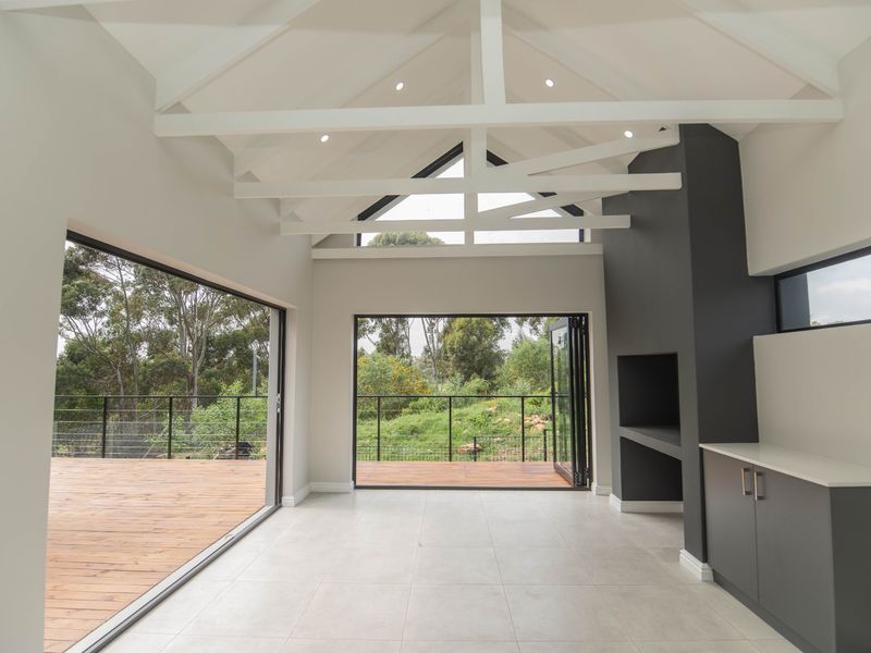 Spacious living area featuring a vaulted ceiling with exposed beams, built-in fireplace, and large bi-fold doors opening onto a wooden deck with scenic views.