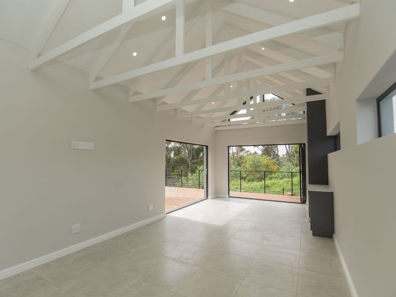 Spacious living area featuring high vaulted ceilings with exposed white trusses, large bi-fold doors opening to a deck, and modern tiled flooring.