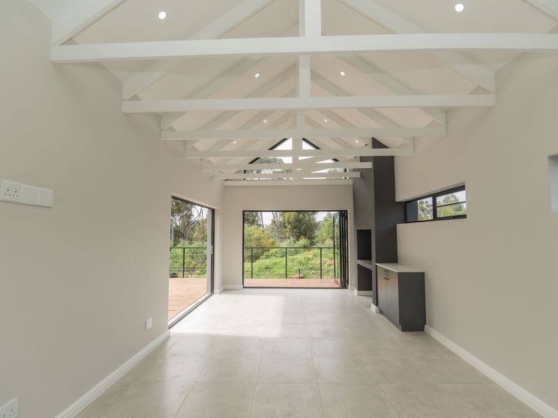 Spacious open-plan living area featuring high vaulted ceilings with exposed trusses, tiled floors, a built-in fireplace, and large stacking doors opening to a deck.