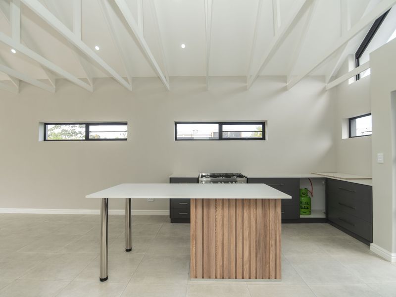 Modern kitchen featuring exposed white rafters, tiled flooring, a central island, and dark cabinetry with a gas hob.