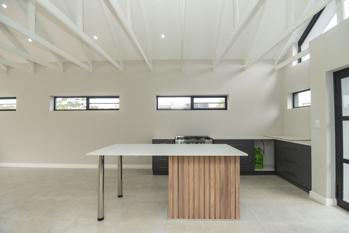 Modern kitchen featuring exposed white rafters, tiled flooring, a central island, and dark cabinetry with a gas hob.