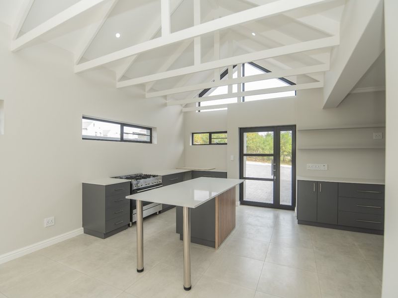 Modern kitchen featuring a central island, gas stove, sleek cabinetry, and high vaulted ceilings with exposed white trusses, creating a bright and airy space.