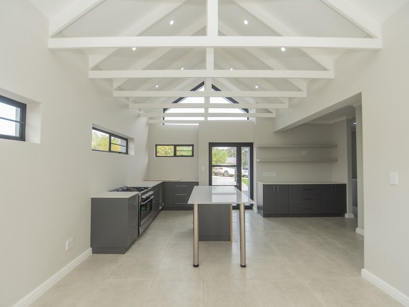 Modern kitchen featuring a vaulted ceiling with exposed rafters, dark grey cabinetry, a central island, and high-quality tiled flooring in an open-plan layout.