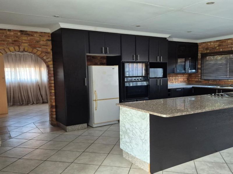Spacious kitchen featuring dark cabinetry, granite countertops, a central island, and rustic exposed brick walls with an arched entryway.