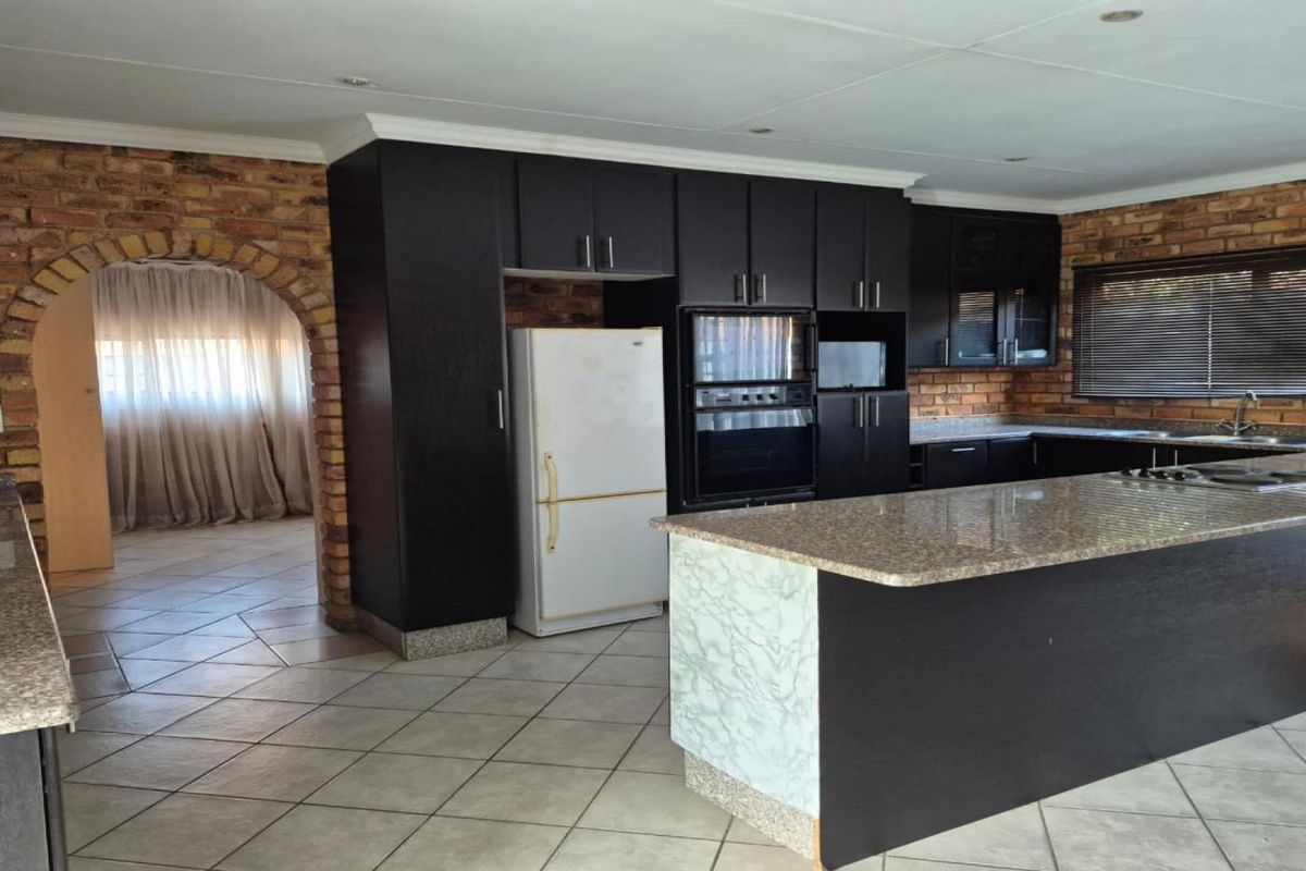 Spacious kitchen featuring dark cabinetry, granite countertops, a central island, and rustic exposed brick walls with an arched entryway.