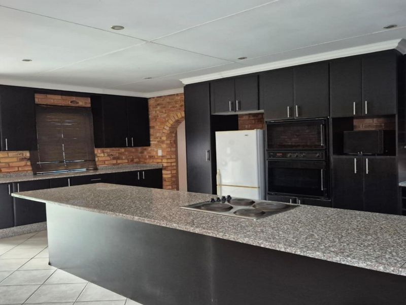 Spacious kitchen featuring dark cabinetry, granite countertops, a central island with a built-in hob, and exposed brick accents.
