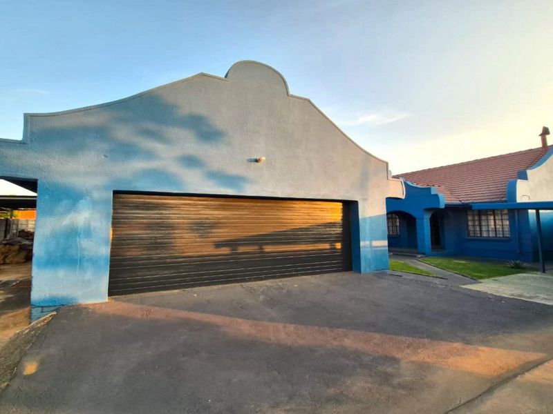 Front view of the property featuring a large garage, asphalt driveway, and a carport, showcasing the building's exterior facade and roof structure.