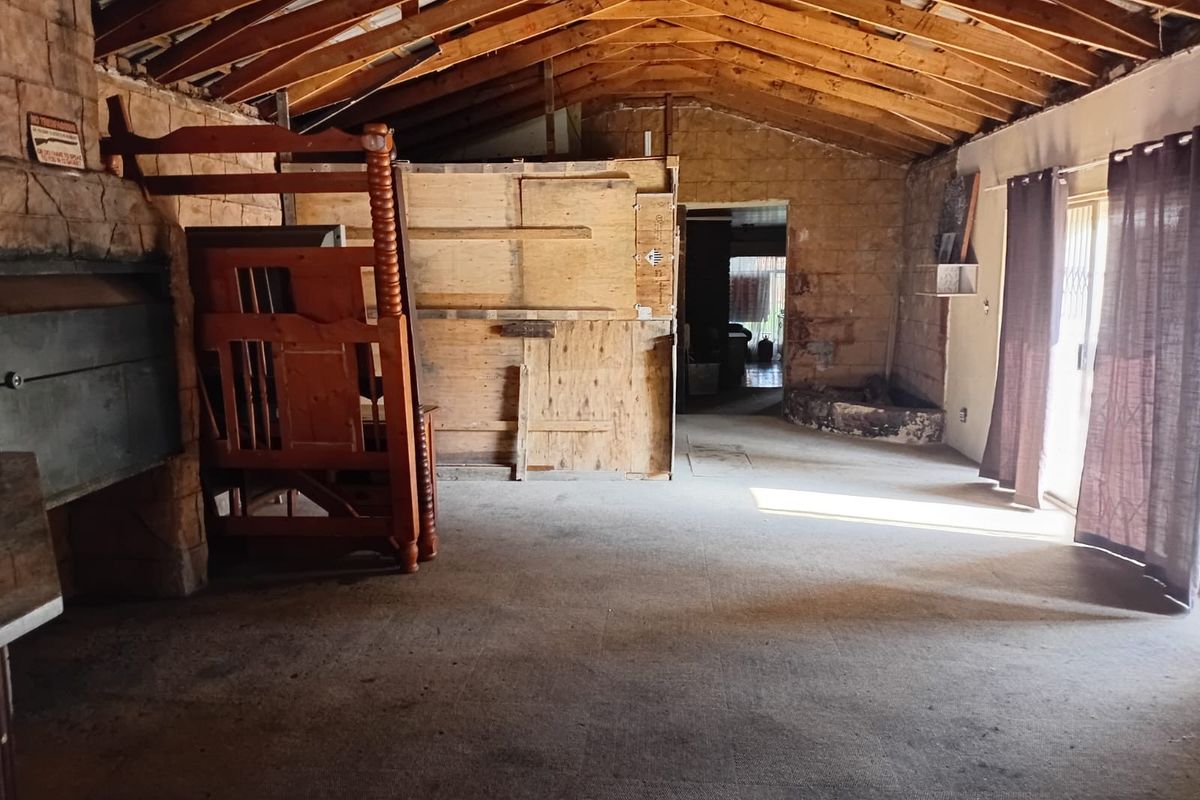 Spacious living area featuring exposed timber roof trusses, stone wall cladding, and a built-in fireplace, offering significant potential for renovation and modernization.