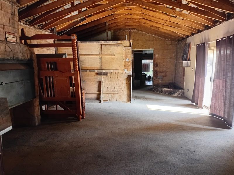 Spacious living area featuring exposed timber roof trusses, stone wall cladding, and a built-in fireplace, offering significant potential for renovation and modernization.