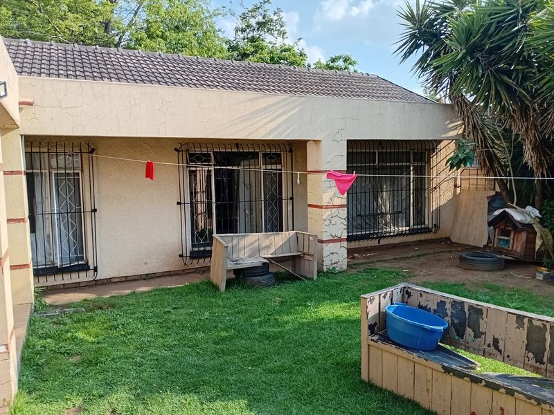Rear view of the house featuring a tiled roof, security bars on windows, and sliding door access to the garden area.