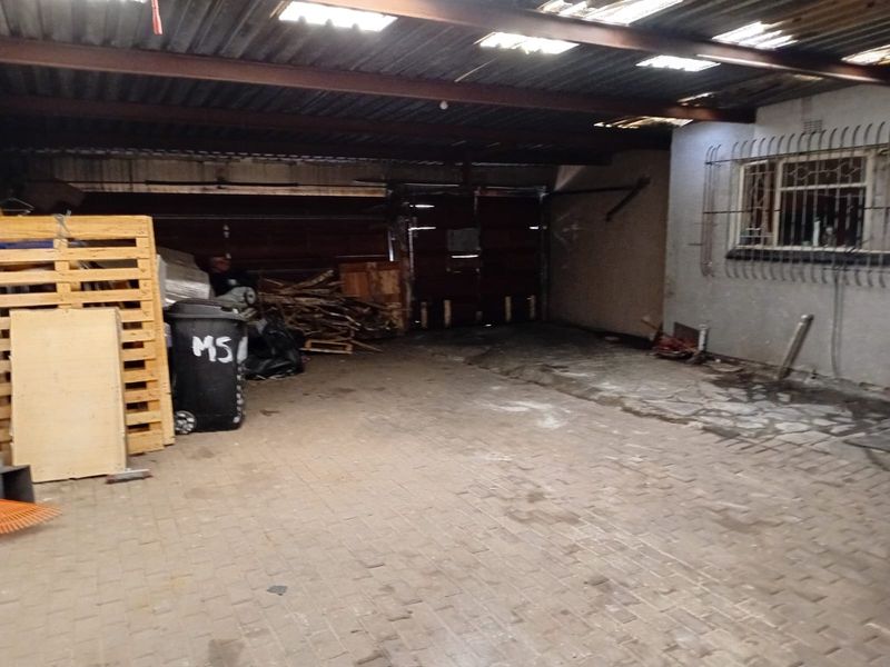 A spacious, utilitarian garage area featuring paved flooring, a corrugated metal roof, and security bars on the adjacent window.