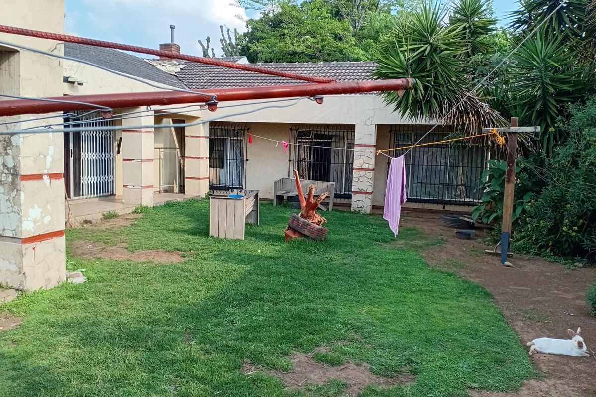 Rear view of the house featuring a lawn area, security bars on windows, and concrete structural pillars requiring maintenance.