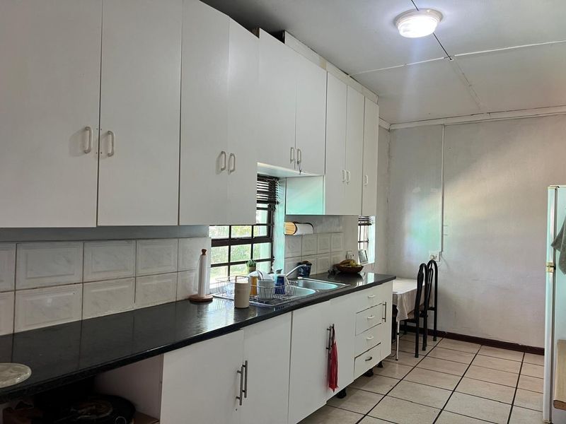 A functional kitchen featuring white built-in cabinetry, a double sink, tiled backsplash, and tiled flooring, offering a practical layout for daily use.