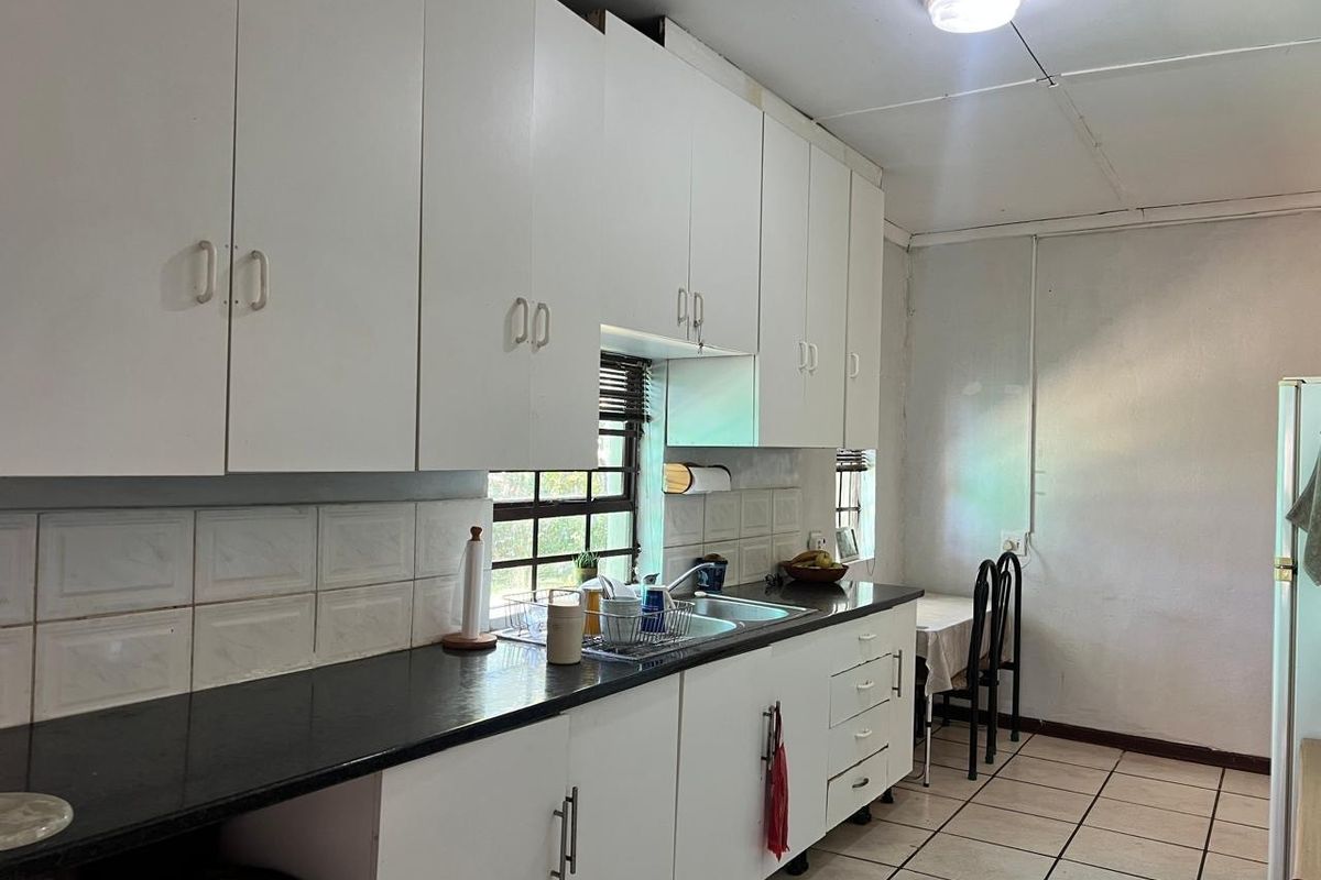 A functional kitchen featuring white built-in cabinetry, a double sink, tiled backsplash, and tiled flooring, offering a practical layout for daily use.