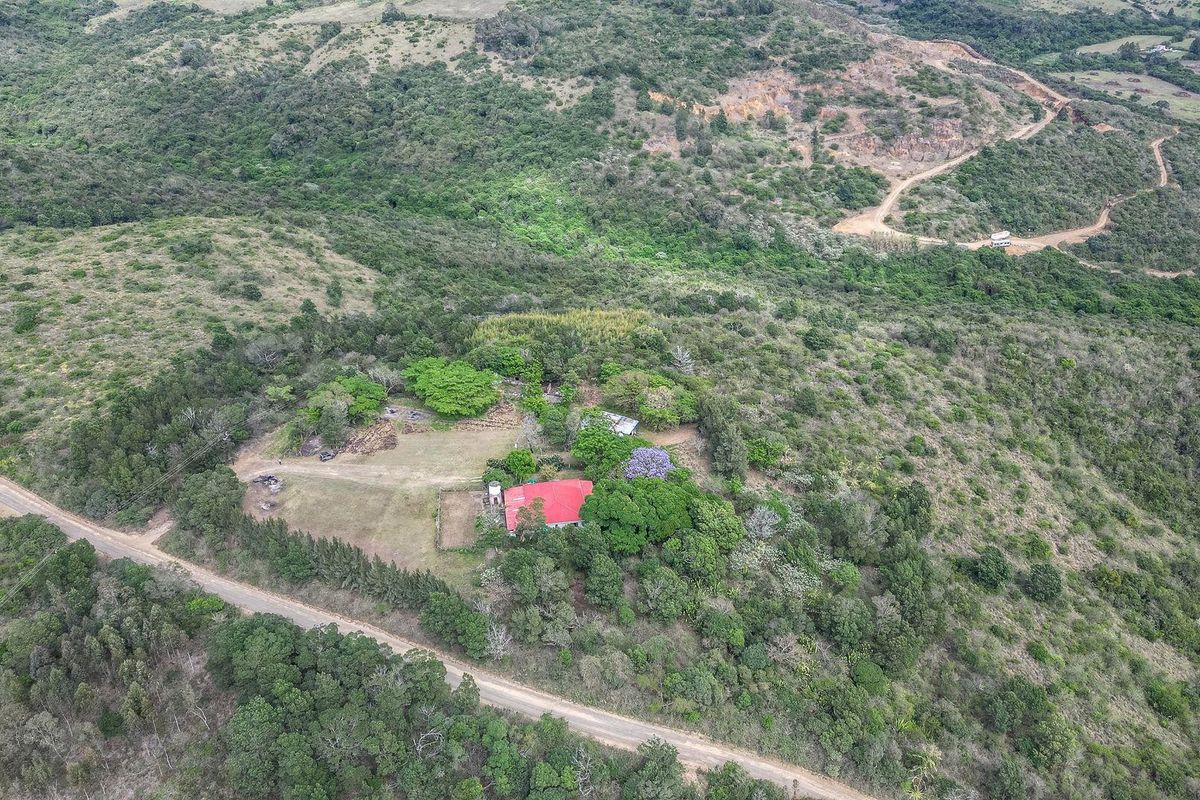 Aerial view of a rural farm property featuring a main dwelling with a red metal roof, surrounded by extensive natural vegetation and access roads.