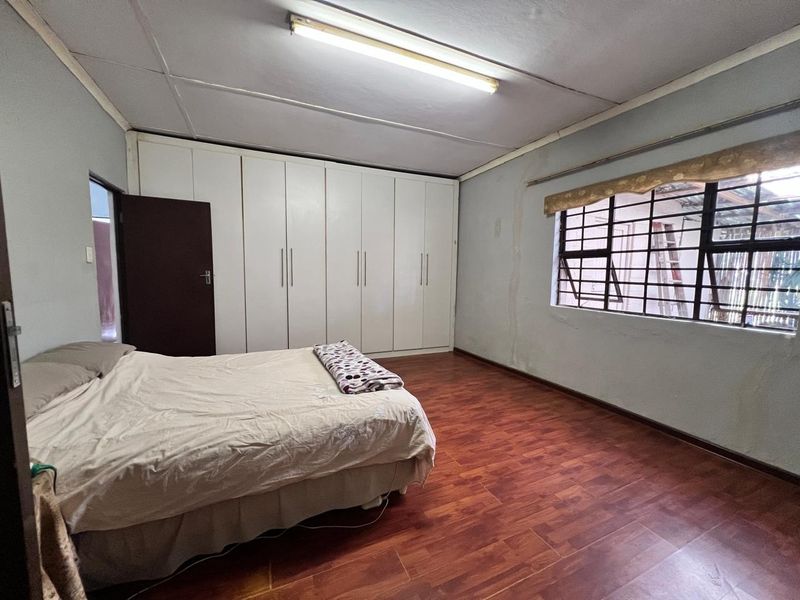 Spacious bedroom featuring laminate flooring, extensive built-in cupboards, and security bars on the window, offering a functional layout with potential for cosmetic updates.