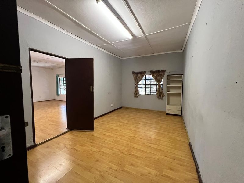 A vacant bedroom featuring laminate flooring, neutral wall finishes, and a window with security bars, offering a blank canvas for potential updates.