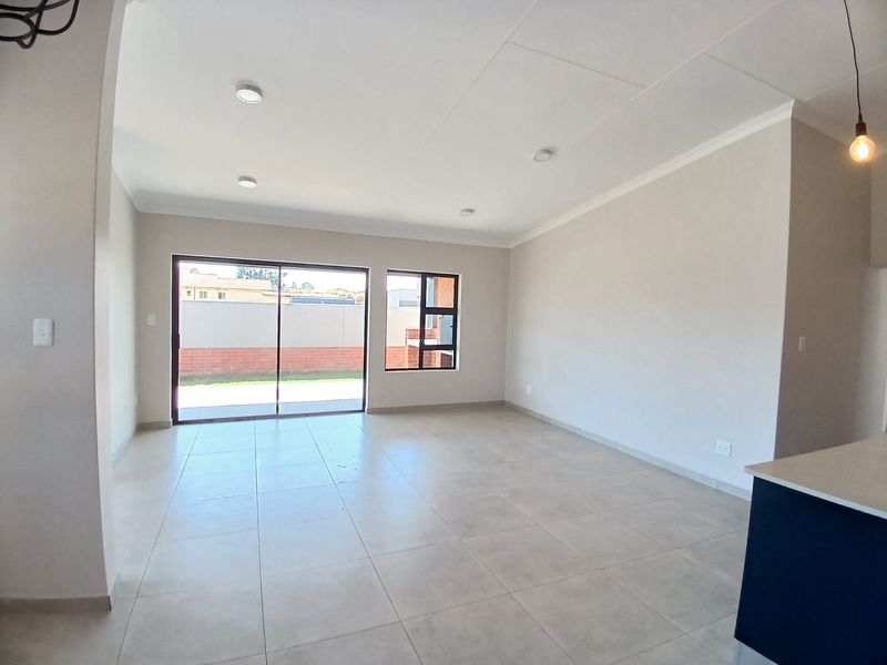 A bright, empty open-plan living area featuring neutral tiled flooring, recessed lighting, and large sliding glass doors leading to the rear exterior.