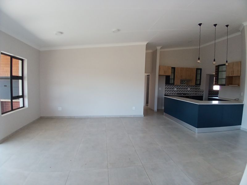 Spacious open-plan living area featuring neutral tiled flooring, recessed lighting, and a modern kitchen with a breakfast island and contemporary cabinetry.