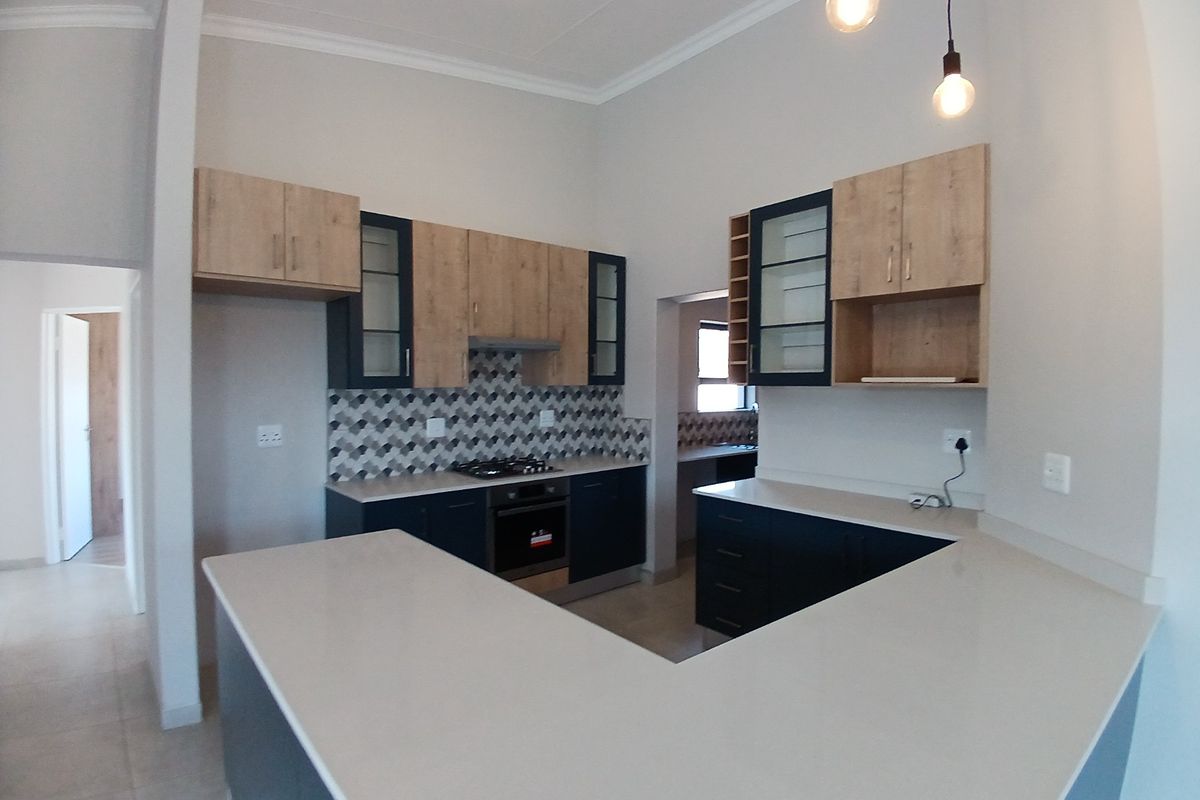 Modern kitchen featuring two-tone cabinetry, stone countertops, gas hob, built-in oven, and a stylish geometric tiled backsplash with ample workspace.