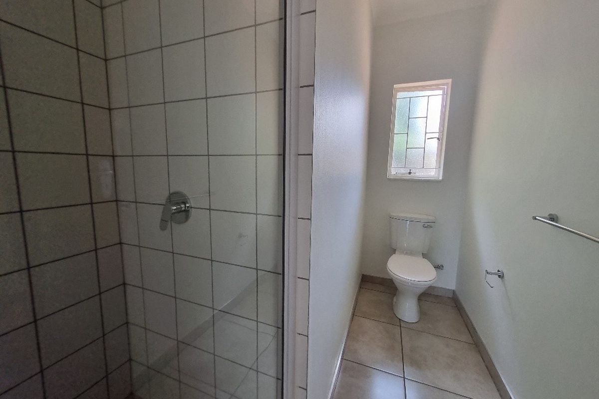 A functional bathroom featuring a tiled shower enclosure, a standard toilet, and tiled flooring, providing a clean and practical space.