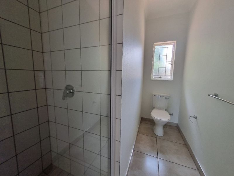 A functional bathroom featuring a tiled shower enclosure, a standard toilet, and tiled flooring, providing a clean and practical space.
