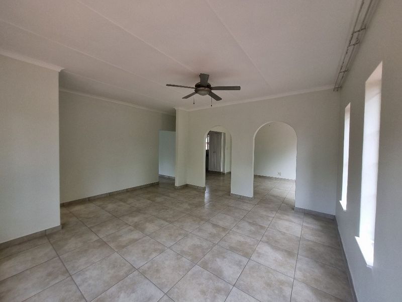 Spacious, empty living area featuring neutral tiled flooring, a ceiling fan, and architectural archways leading to adjacent rooms.