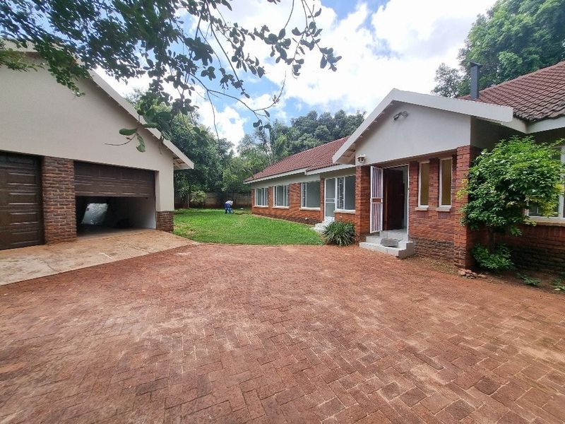 Front view of a brick-faced house featuring a spacious paved driveway, a double garage, and a well-maintained garden area.