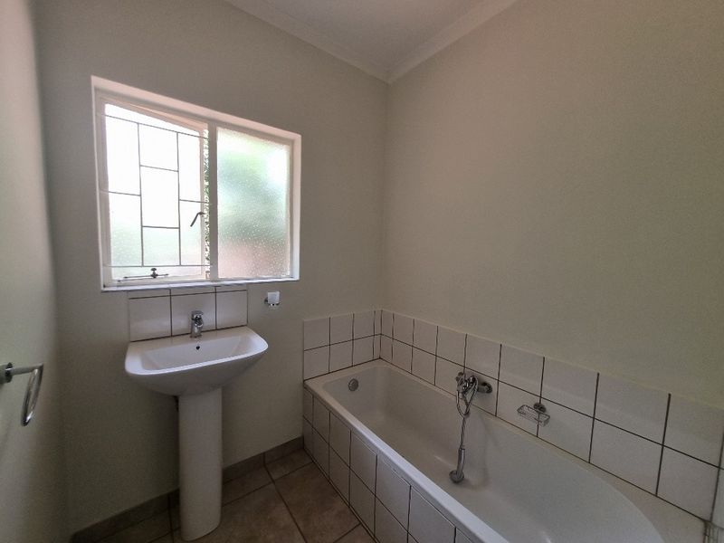 A clean, functional bathroom featuring a pedestal basin, a built-in bathtub with tiled surround, and a window with security bars.